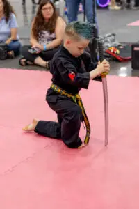 young boy kneeling with a martial arts sword